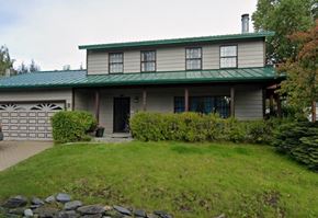 Anchorage house for rent - A house with a green roof and a grey body with a black door and windows.