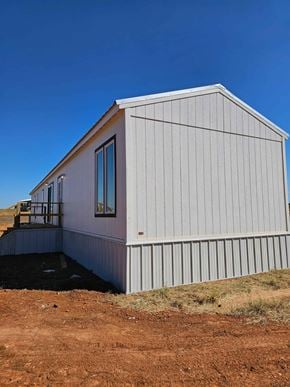 Guthrie house for rent - A small white building with a window and a door is situated on a dirt area.