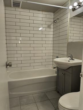 Brantford apartment for rent - A white tiled bathroom with a bathtub, toilet, and sink.