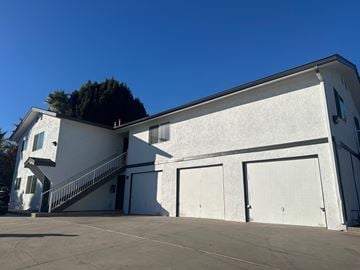 Vista apartment for rent - A white building with a black roof and a tree behind it.