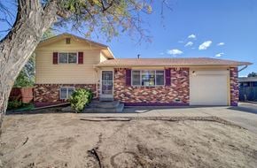 Colorado Springs house for rent - A house with a yellow siding and a brick wall is shown.