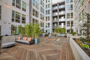 Oakland apartment for rent - A wooden deck with a bench and plants in the foreground and apartment buildings in the background.