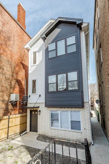 Chicago apartment for rent - A two-story building with a grey facade stands between a red brick building and a brown wooden fence.