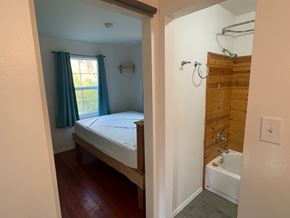 Hyampom house for rent - A bedroom with a bed, a window with blue curtains, and a wooden wall.