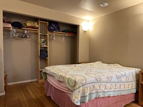 Sitka house for rent - A bedroom with a bed, wooden shelves, and clothes hanging on hangers.