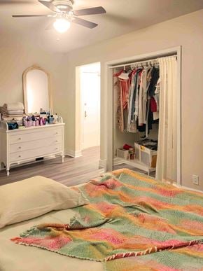 Winnipeg apartment for rent - A bedroom with a bed, a dresser, a mirror, a ceiling fan, and a closet with clothes.
