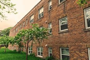 Winnipeg apartment for rent - A red brick building with green trees in front.