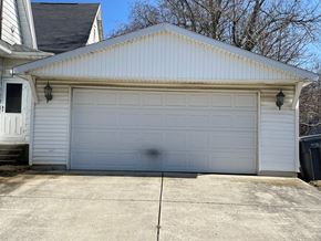 Lima house for rent - A white garage door is closed and there is a black trash can to the right of the garage.