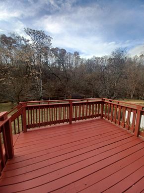 Clarksville house for rent - A red wooden deck with a railing and trees in the background.