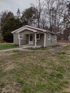 Armuchee house for rent - A small house with a porch is surrounded by a grassy area and trees.