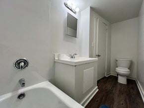 Glassport house for rent - A white bathroom with a tub, sink, mirror, and toilet.