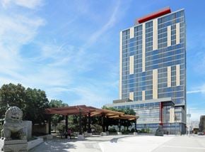 Philadelphia apartment for rent - A modern building with a red stripe on the top floor is surrounded by trees and a stone lion statue.