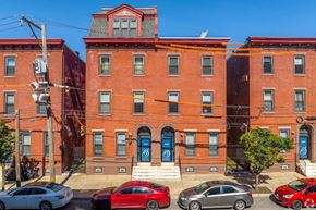 Philadelphia apartment for rent - A red brick building with a blue door and a red car parked in front.