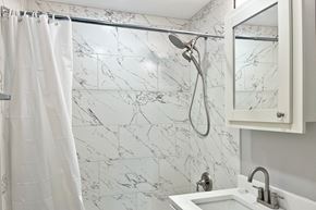 Forest Park apartment for rent - A white shower curtain hangs over a marble shower wall.