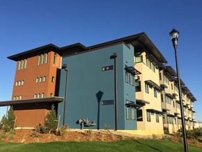 Longmont apartment for rent - A modern building with a blue and brown facade stands under a clear blue sky.