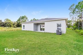 Palm Bay house for rent - A white house with a green door and a window is surrounded by green grass and trees.