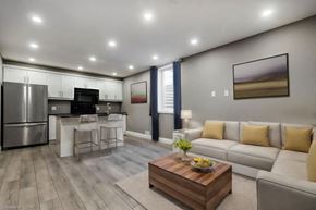 Kitchener apartment for rent - A modern kitchen with a refrigerator, microwave, and oven, with a dining area and a living room with a couch and a coffee table.