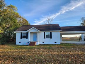 Statesboro house for rent - A small white house with a blue door stands alone in a grassy field.
