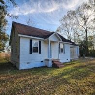 Statesboro house for rent - A small white house with a brown roof sits in a grassy field.