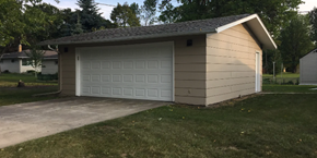 Moorhead house for rent - A tan garage with a white door is situated in a grassy area.