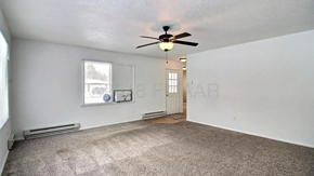 Moorhead house for rent - A spacious room with a ceiling fan and carpeted floor.