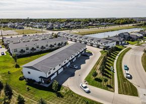 West Fargo townhouse for rent - A large white building with a grey roof is surrounded by a grassy area and a road with cars.