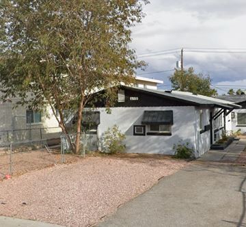 Las Vegas apartment for rent - A white building with a black awning is surrounded by a gravel area and a tree.