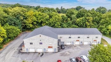 Frederick apartment for rent - A large stone building with a grey roof is surrounded by a parking lot and trees.