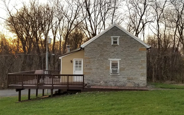 Frederick house for rent - A small house with a porch and a deck is surrounded by trees.