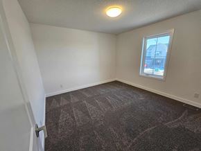 Airdrie house for rent - A room with a carpeted floor and a window showing a building outside.