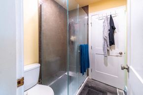 Victoria apartment for rent - A bathroom with a toilet, a glass shower door, and a white door.