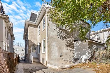 Philadelphia apartment for rent - A grey house with a white door and windows is surrounded by a fence and trees.