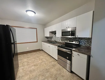 Fargo apartment for rent - A kitchen with white cabinets and black appliances.