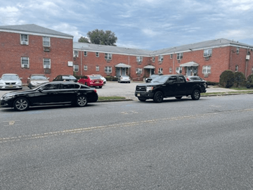 Paterson apartment for rent - A black car is parked on the side of a street in front of a brick apartment building.
