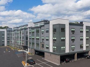 Bergenfield apartment for rent - A parking lot in front of a grey building with cars parked.