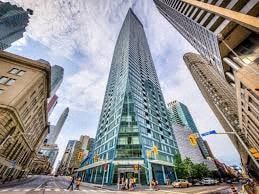 Toronto apartment for rent - A tall, modern glass skyscraper stands in the middle of a city street.