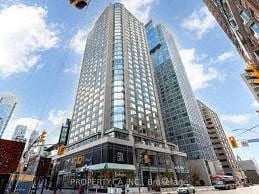 Toronto apartment for rent - A tall building with a glass facade stands in the middle of a city street.