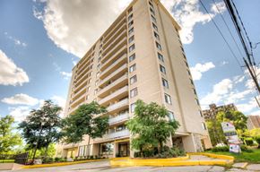 Toronto apartment for rent - A tall beige apartment building with a yellow entrance and trees in front.