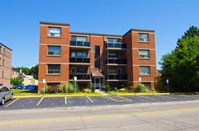 Hamilton apartment for rent - A multi-story brick building with a parking lot in front.