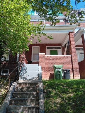 Baltimore apartment for rent - A red brick house with a green trash can and a tree in front.