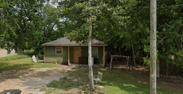 El Campo apartment for rent - A green house with a brown roof and a brown door is surrounded by trees.