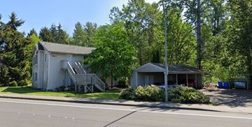 Bellingham apartment for rent - A white house with a porch and a garage is surrounded by trees.