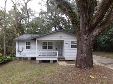 Tallahassee house for rent - A small white house with a porch and a tree in front.