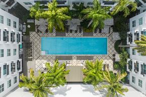 Pompano Beach apartment for rent - A swimming pool surrounded by palm trees and white buildings.