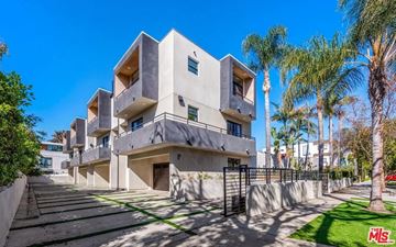Los Angeles apartment for rent - A modern building with a flat roof and balconies is surrounded by a well-manicured lawn and palm trees.