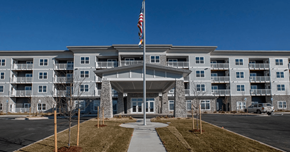 Greeley apartment for rent - A large building with a flag on top and a walkway leading to the entrance.