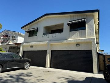 Los Angeles apartment for rent - A black car is parked in front of a two-story building with a garage.