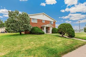 Lakewood apartment for rent - A house with a red brick exterior and a white roof is surrounded by a green lawn and trees.