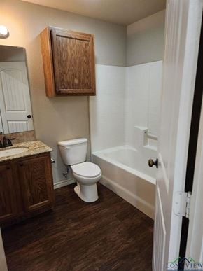 Longview apartment for rent - A white toilet sits in a bathroom with wood cabinets and a white tub.