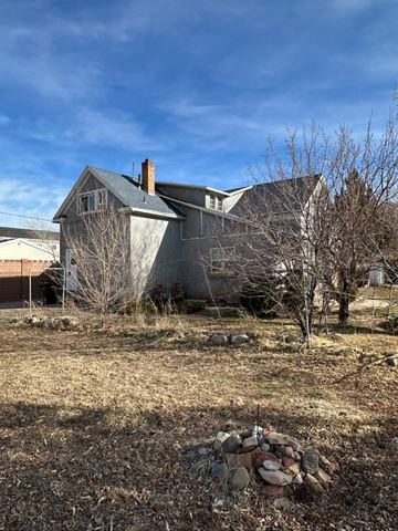 Cedar City house for rent - A house with a grey roof and a chimney is surrounded by a bare tree and a pile of rocks.